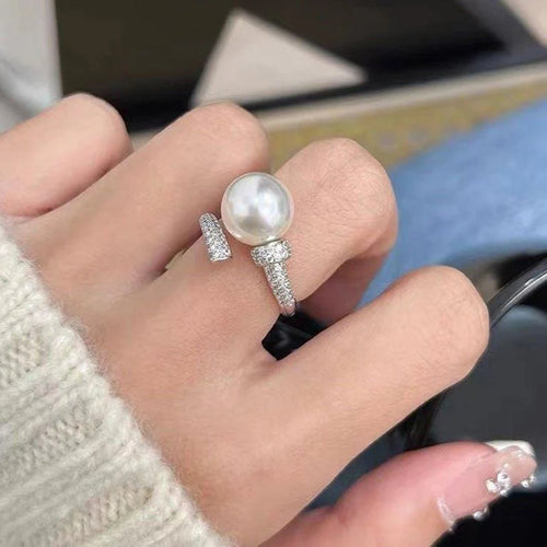 Hand wearing a pearl ring with diamond accents on a blurred background